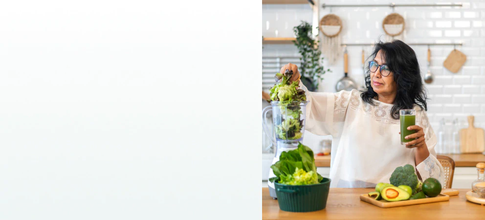 A woman in a kitchen blending leafy greens while holding a green juice, representing the benefits of supplements for cleanse and detox.