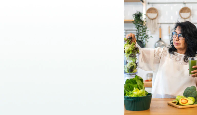 A woman in a kitchen blending leafy greens while holding a green juice, representing the benefits of supplements for cleanse and detox.