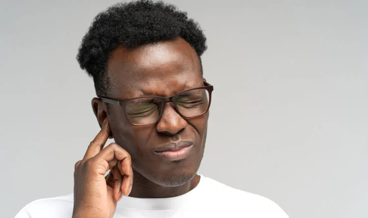 A man pressing his finger to his ear in discomfort, representing the need for supplements for hearing loss.